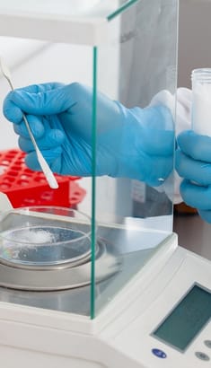 Balanza analítica de laboratorio DAG en uso, pesando una muestra con guantes de nitrilo