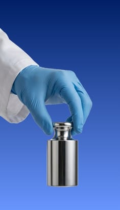Técnico manipulando una masa patrón con guantes para evitar contaminación de la superficie